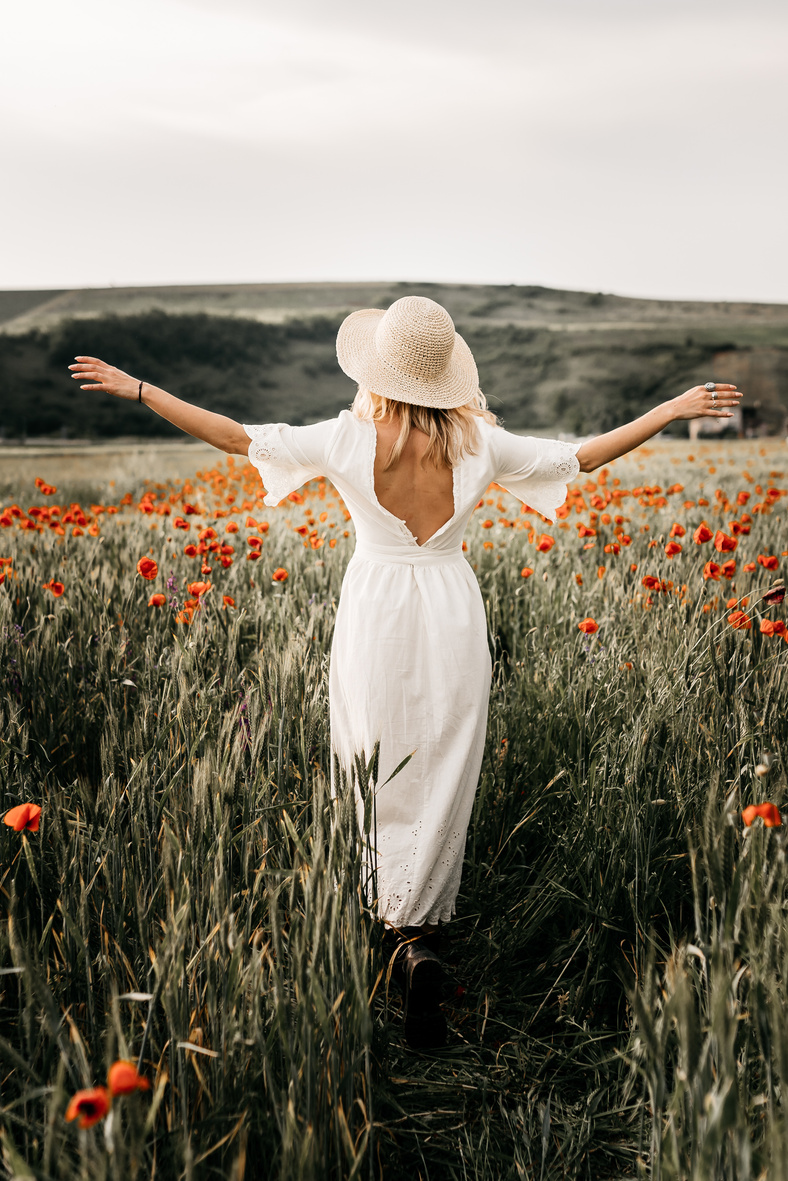 Elegant woman in hat walking in field with flowers